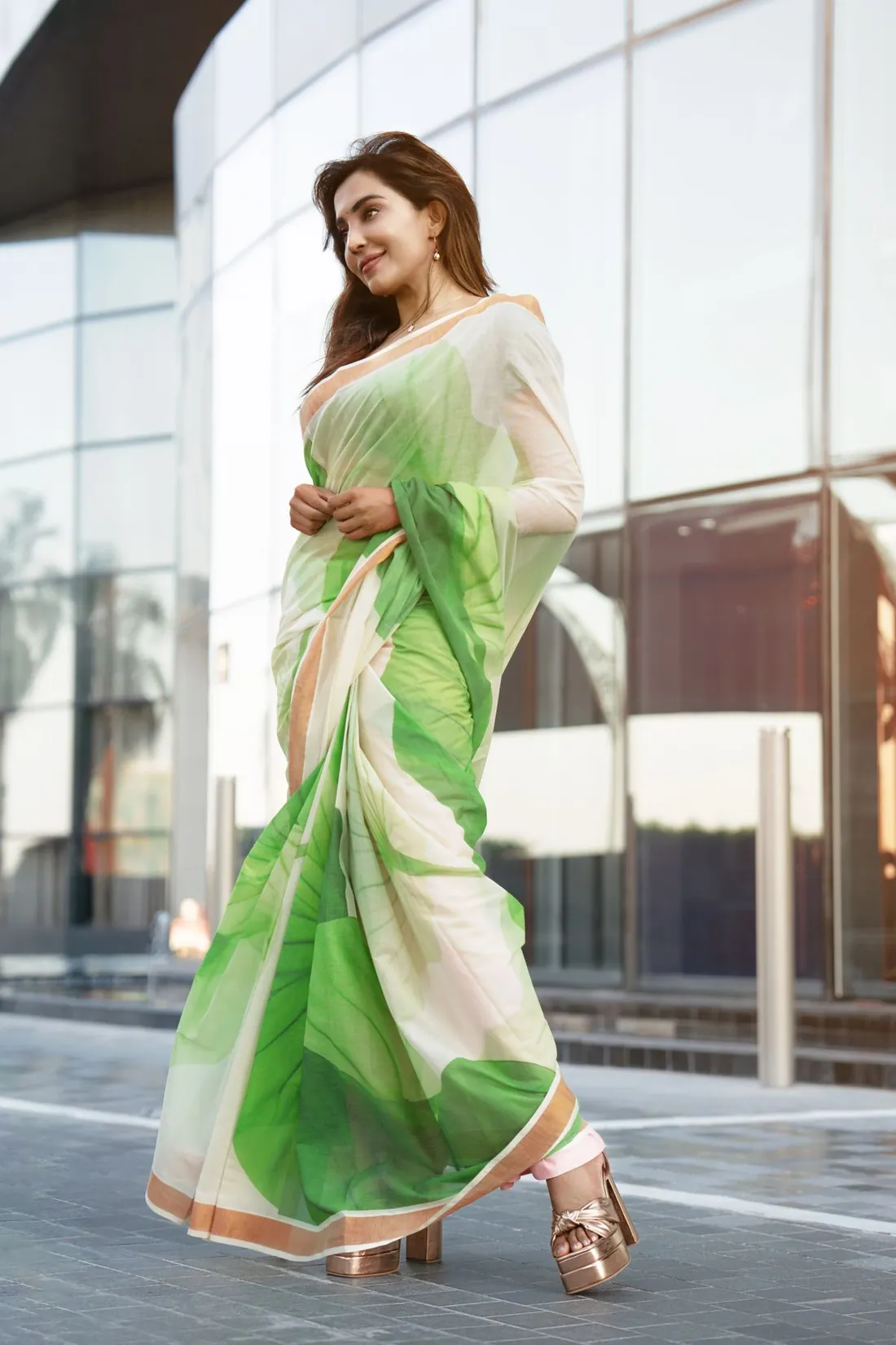 Fashion portrait of a woman in a green sari posing outside a modern glass building